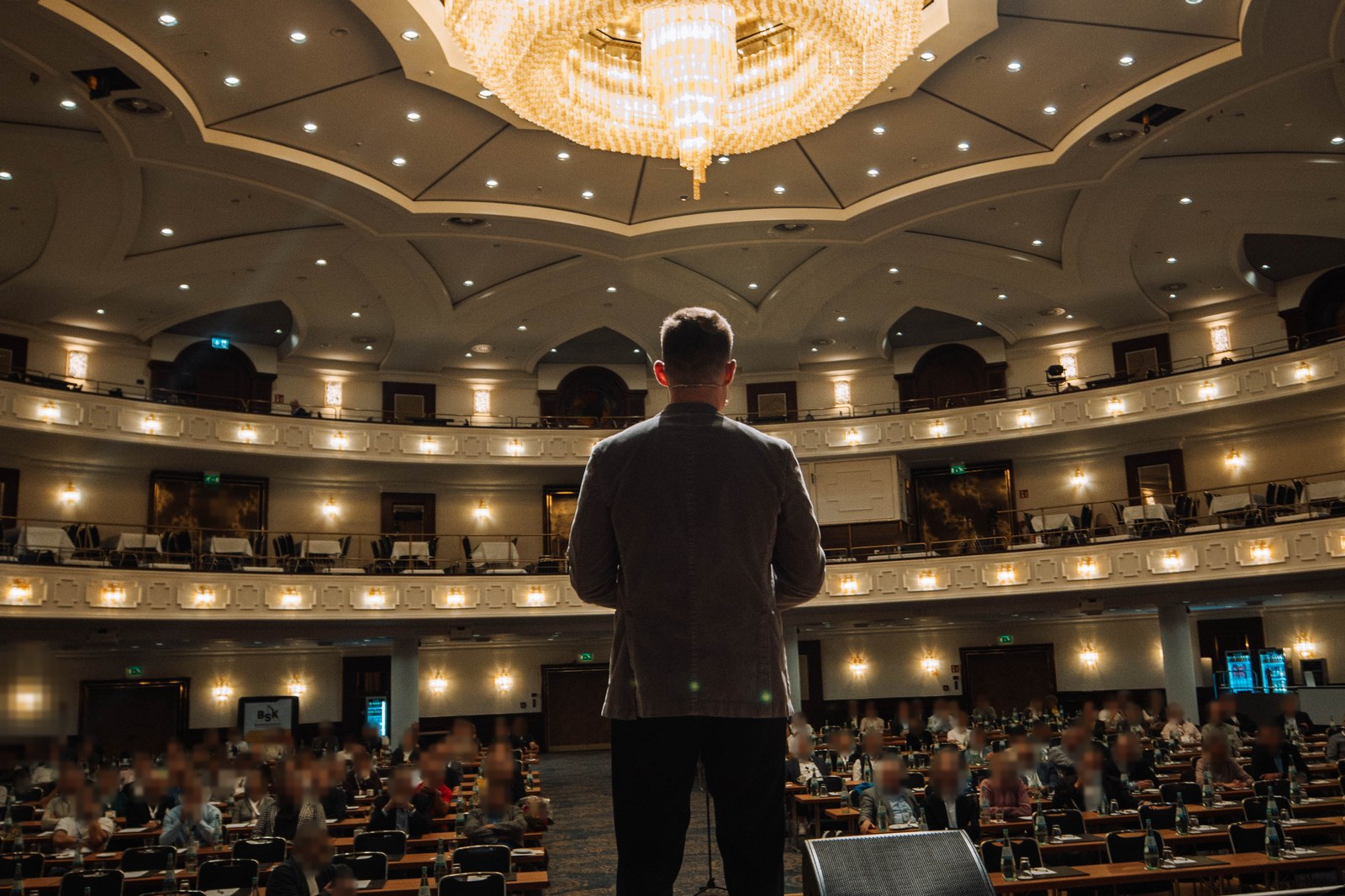 Michael Schaudienst auf der Bühne vor vollem Saal, von hinten fotografiert
